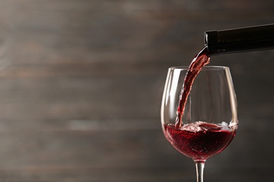 Pouring red wine into glass from bottle against blurred wooden background, closeup. Space for text