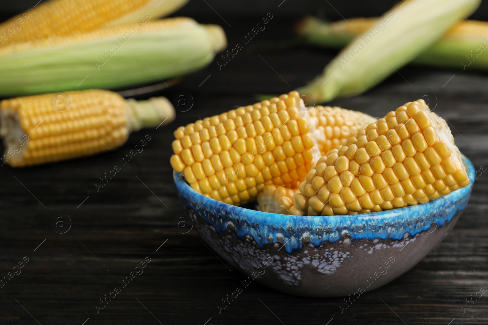 Photo of Bowl with tasty sweet corn cobs on table, closeup