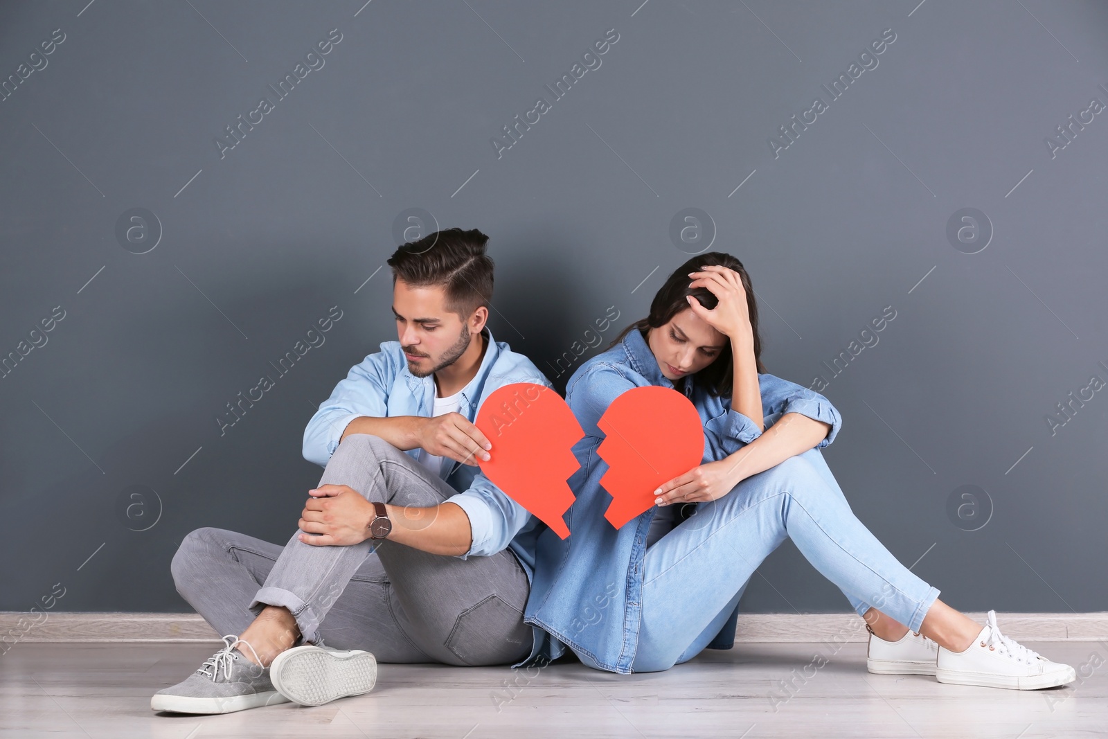Photo of Young couple with torn paper heart indoors. Relationship problems