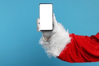 Photo of Merry Christmas. Santa Claus showing smartphone on light blue background, closeup. Mockup for design