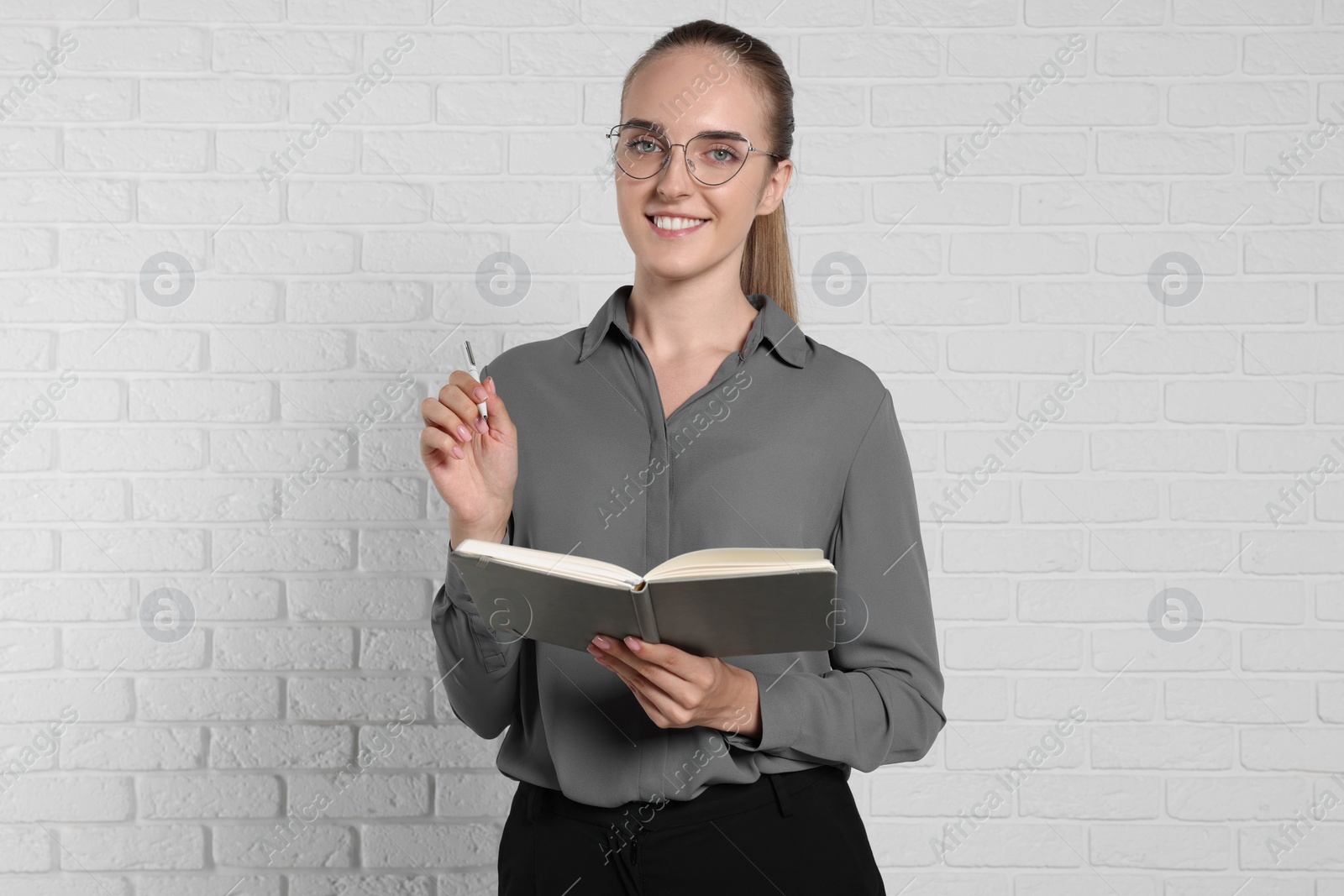 Photo of Happy young secretary with notebook and pen near white brick wall