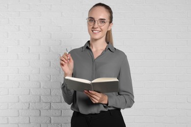 Happy young secretary with notebook and pen near white brick wall