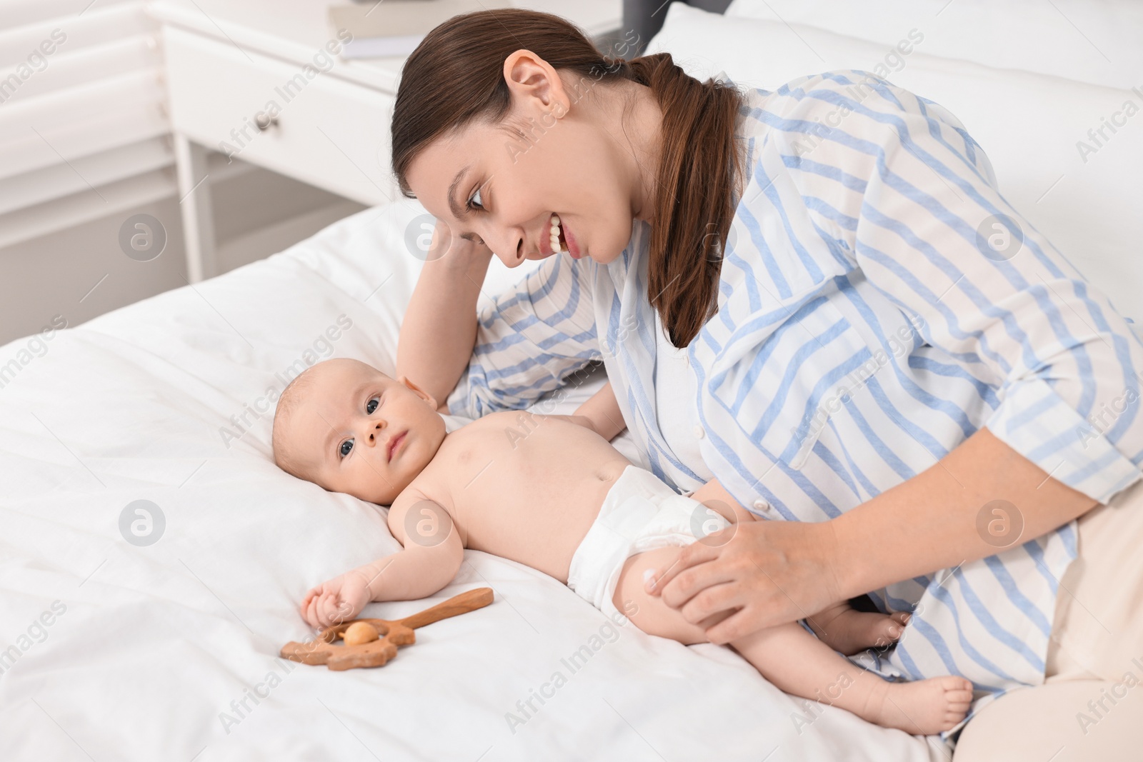 Photo of Happy young woman applying body cream onto baby`s skin on bed