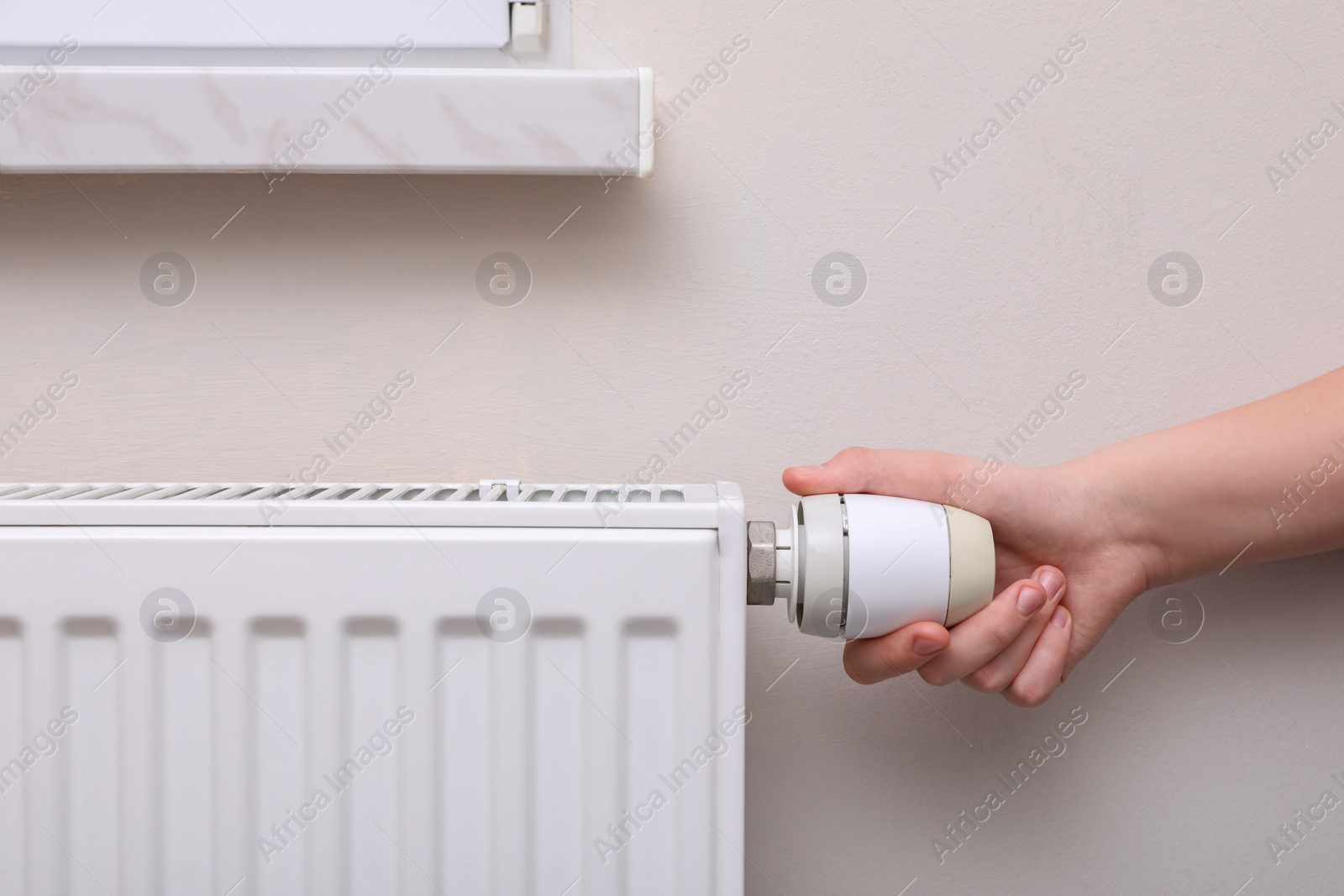 Photo of Girl adjusting heating radiator thermostat near white wall indoors, closeup