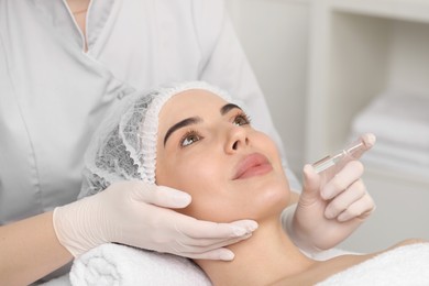 Professional cosmetologist holding skincare ampoule while working with client in clinic, closeup