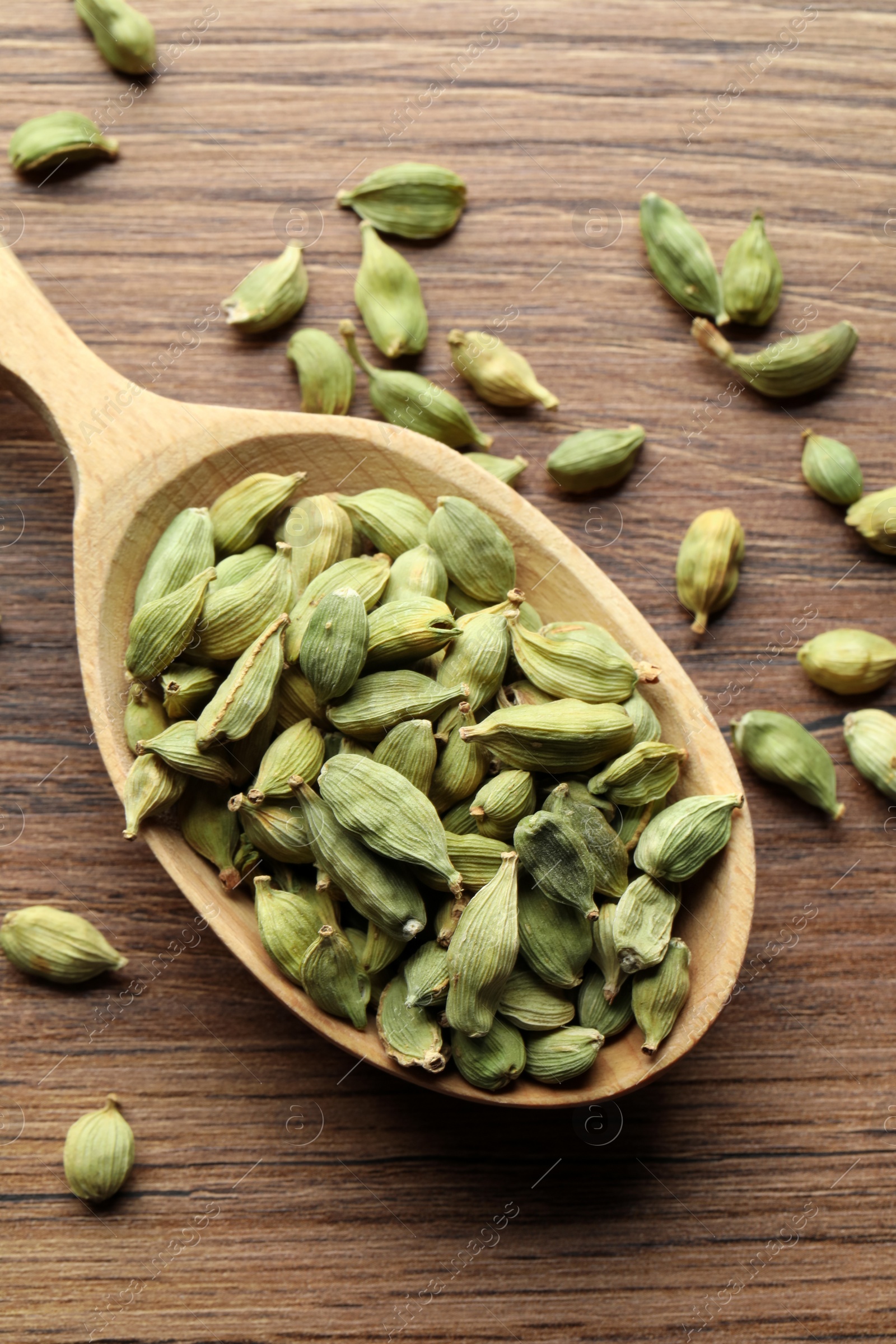 Photo of Spoon with dry cardamom pods on wooden table, top view