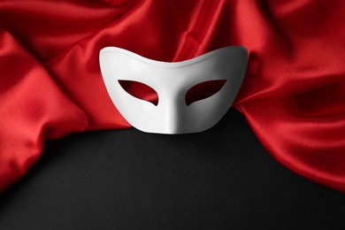 White theatre mask and red fabric on black background, above view. Space for text