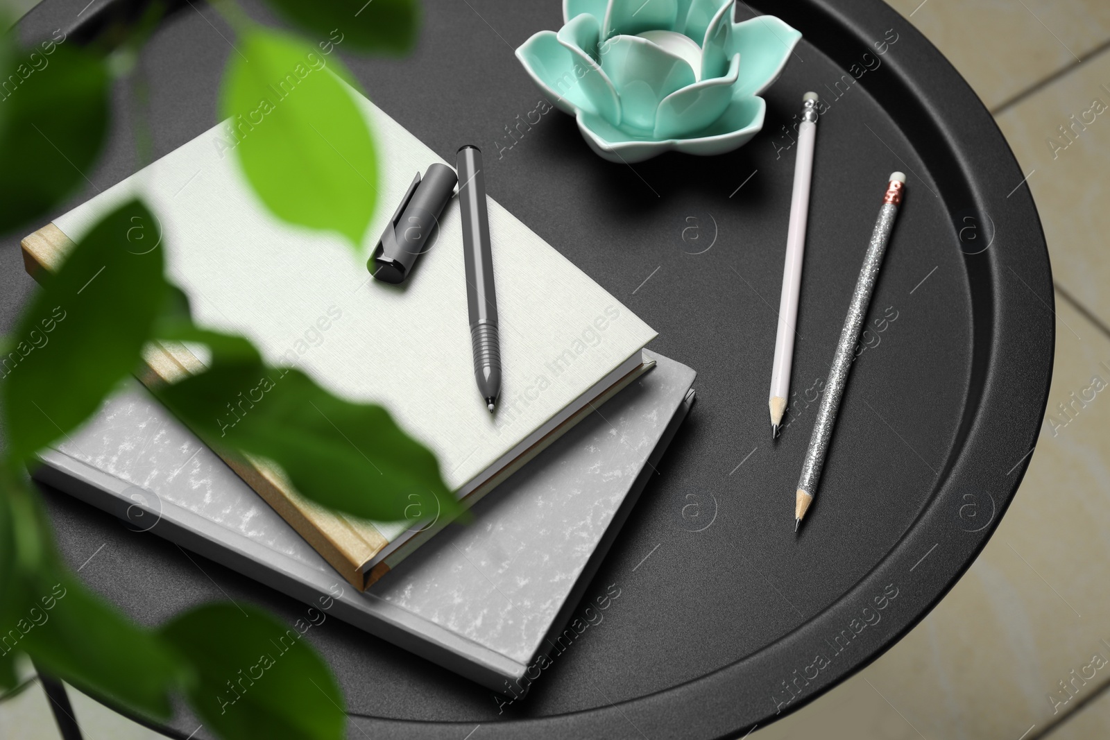 Photo of Notebooks, pen, pencils and decorative holder with candle on round table indoors, closeup