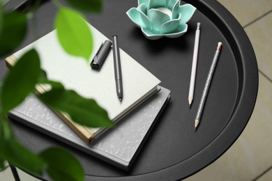 Photo of Notebooks, pen, pencils and decorative holder with candle on round table indoors, closeup