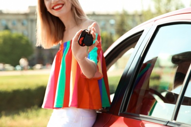 Young woman with car key near automobile outdoors