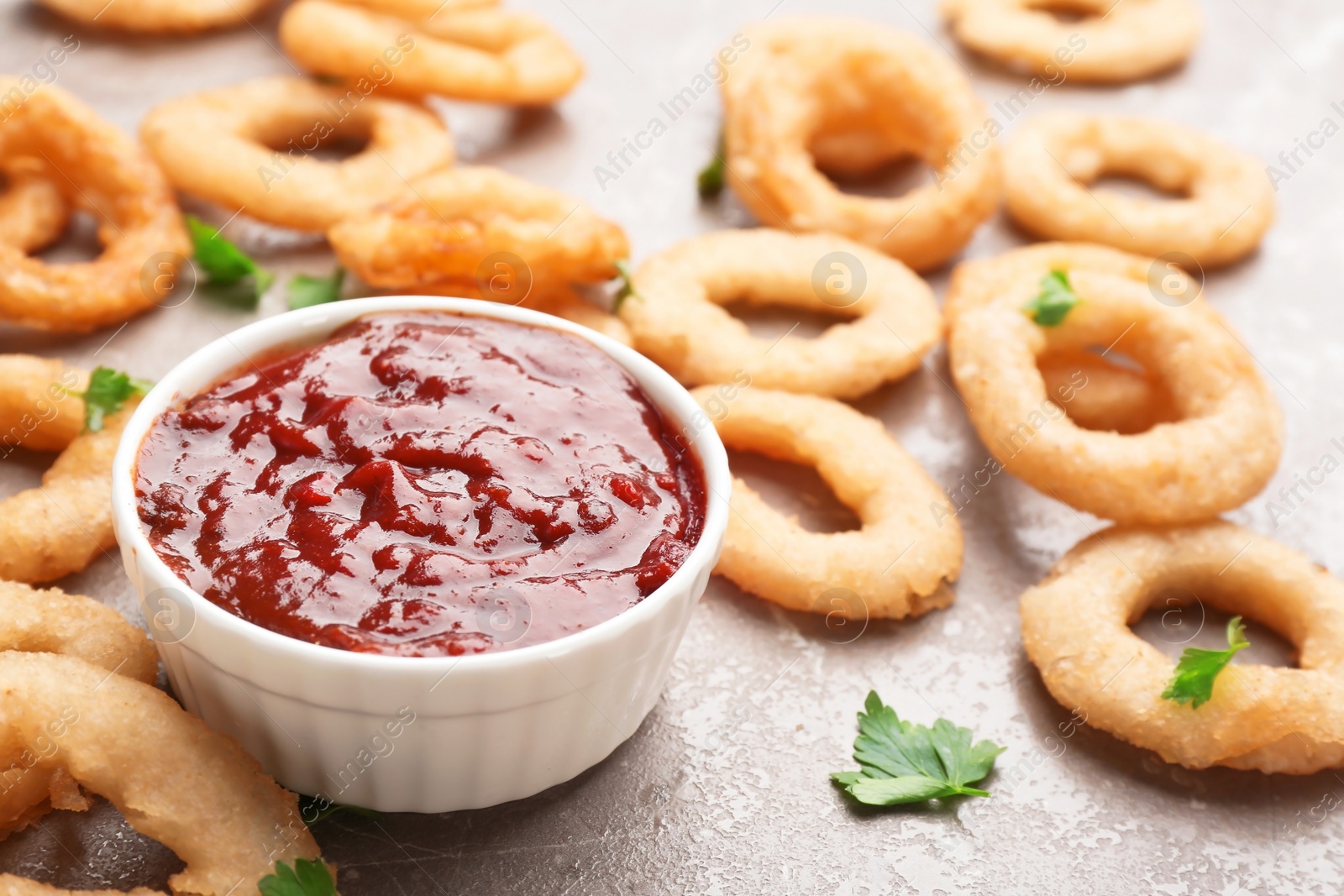 Photo of Fried onion rings and bowl of sauce on grey background, closeup