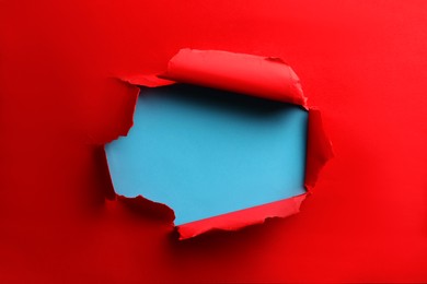 Photo of Hole in red paper on light blue background