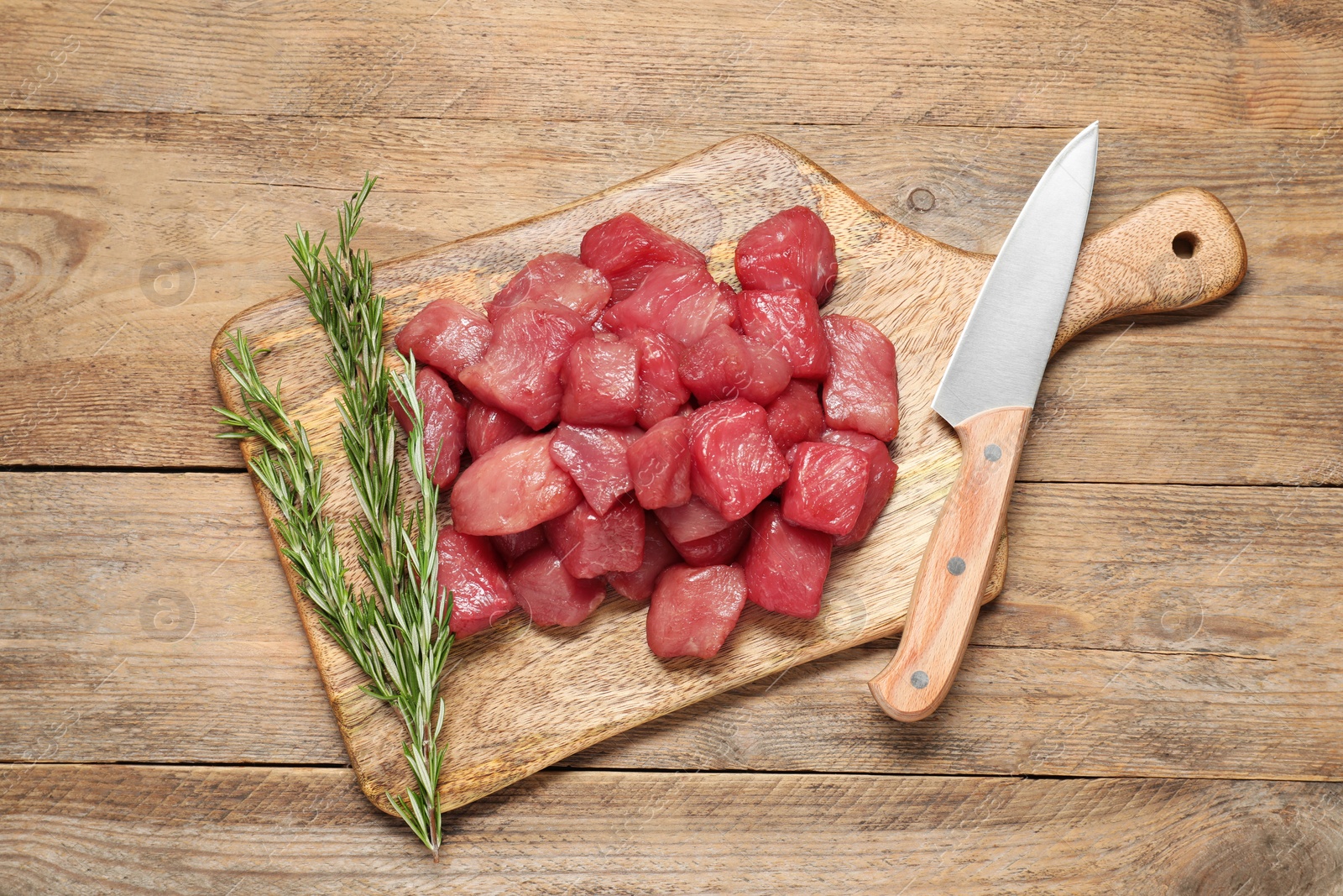 Photo of Cooking delicious goulash. Raw beef meat, rosemary and knife on wooden table, top view