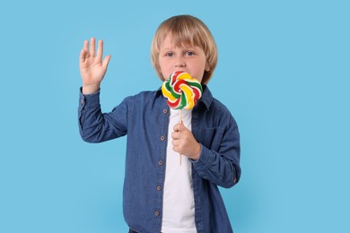 Cute little boy licking colorful lollipop swirl on light blue background