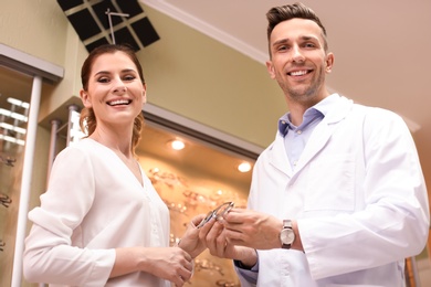 Photo of Male ophthalmologist helping woman to choose glasses in optical store