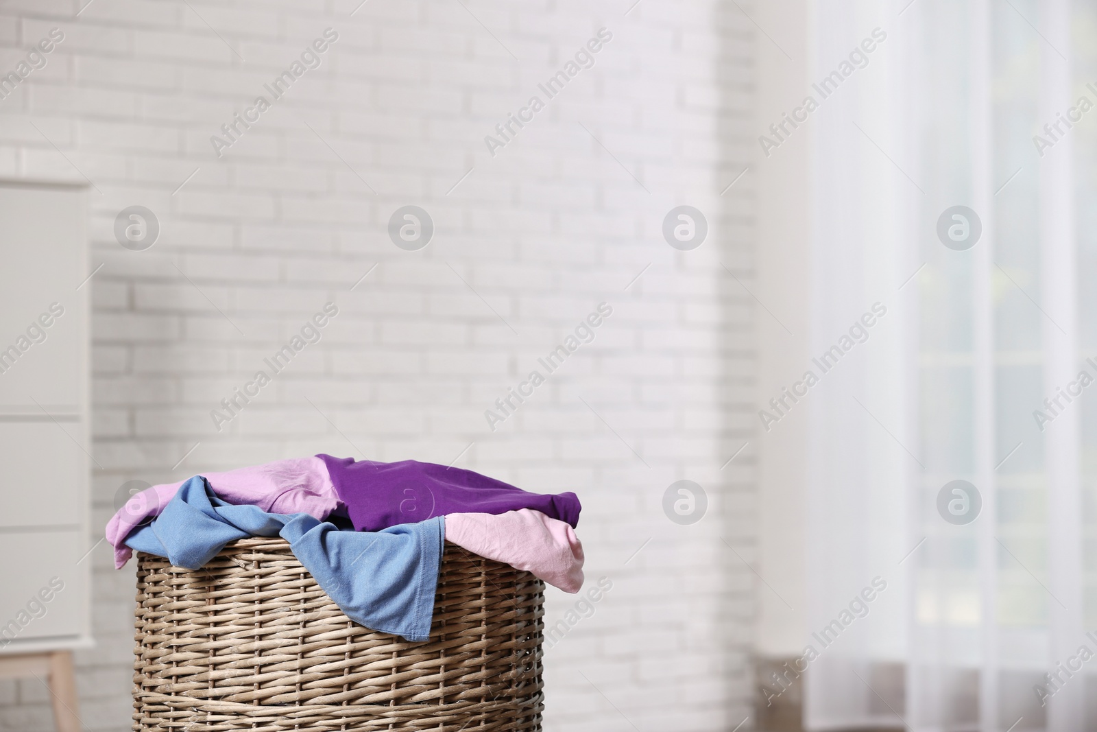 Photo of Laundry basket with dirty clothes in room, space for text