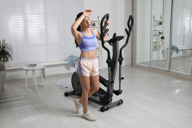 Young woman feeling tired of training on 	
elliptical machine at home