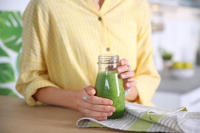 Young woman with bottle of healthy smoothie at table, closeup