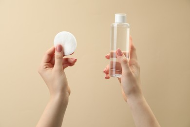 Photo of Woman holding makeup remover and cotton pad on beige background, closeup