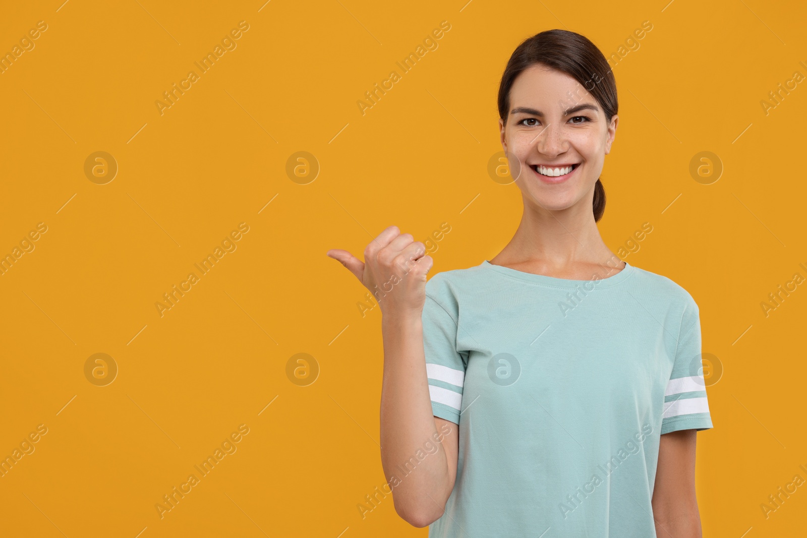 Photo of Special promotion. Happy woman pointing at something on orange background, space for text