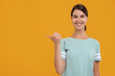 Photo of Special promotion. Happy woman pointing at something on orange background, space for text