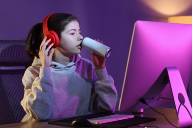 Girl with energy drink playing computer game at home