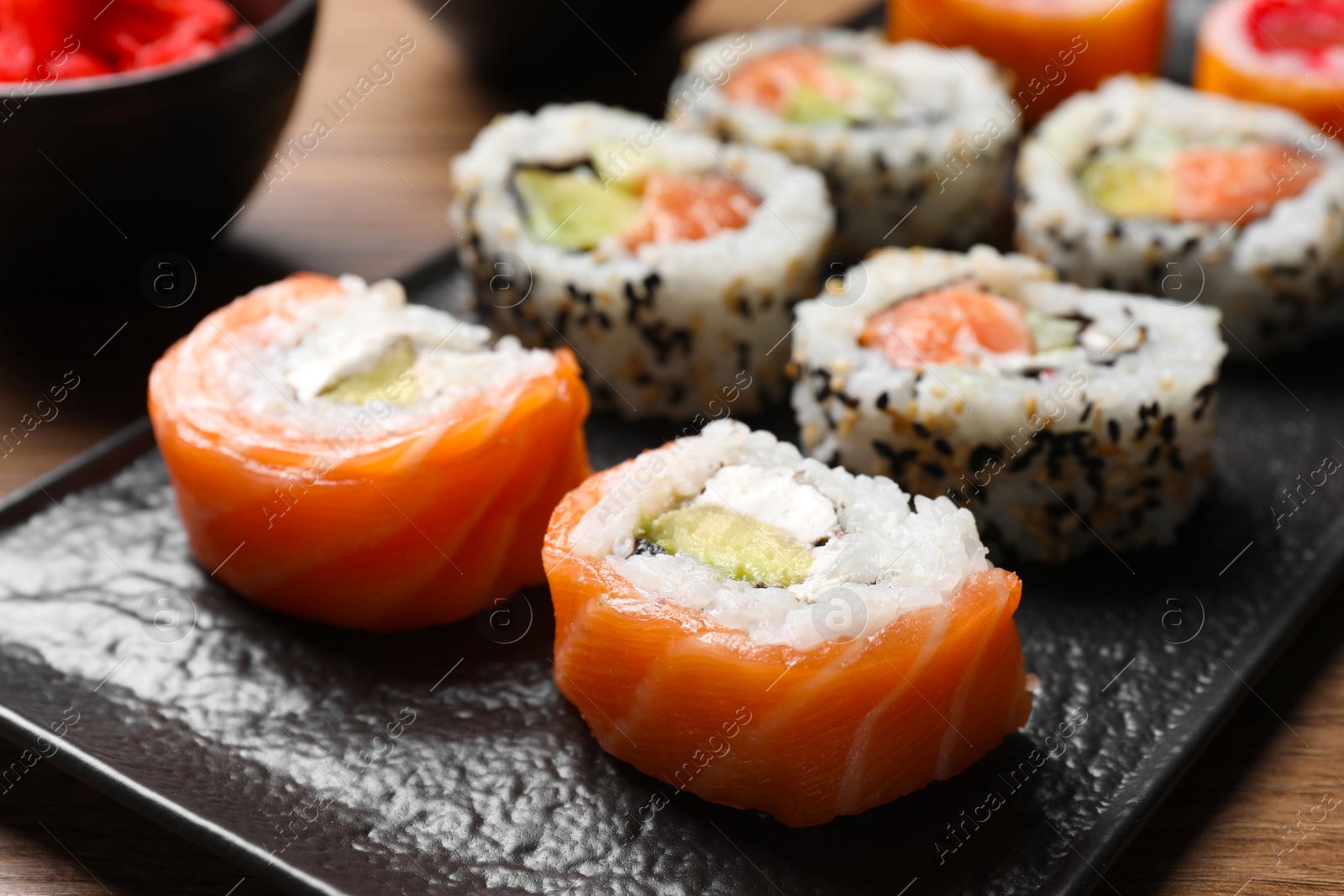 Photo of Delicious sushi rolls on black plate, closeup