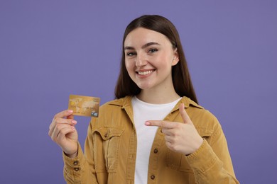 Happy woman pointing at credit card on purple background