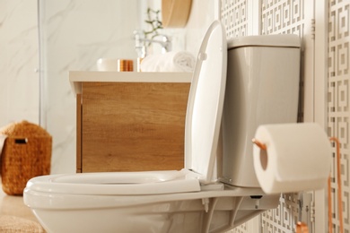 Photo of Toilet bowl near wooden screen in modern bathroom interior