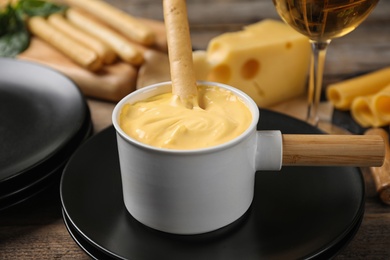 Photo of Pot of tasty cheese fondue and products on wooden table