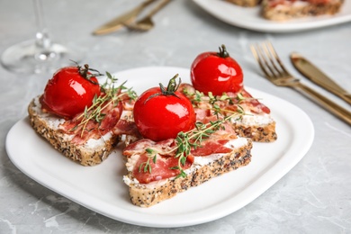 Photo of Plate of delicious bruschettas with prosciutto on grey table