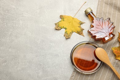 Flat lay composition with tasty maple syrup and dry leaves on light grey table, space for text