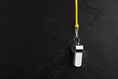 Photo of Referee equipment. Metal whistle on black textured background, closeup and space for text