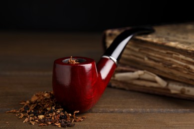 Photo of Smoking pipe and dry tobacco on wooden table, closeup