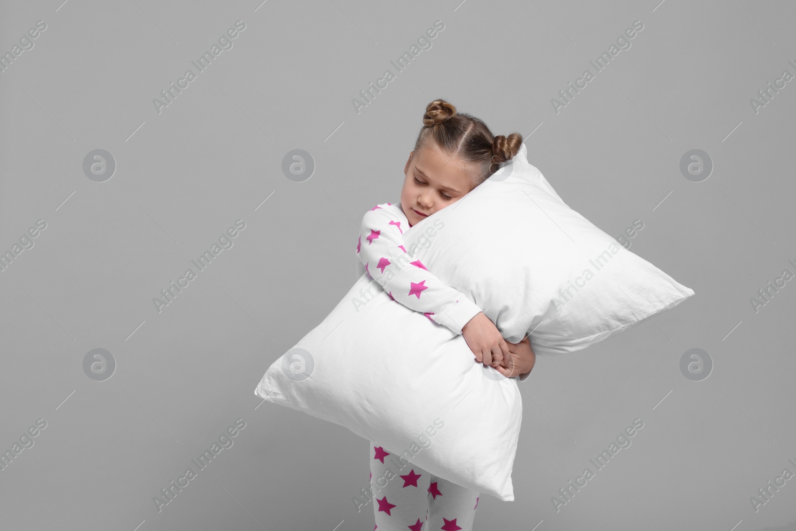 Photo of Girl in pajamas hugging pillow on gray background, space for text