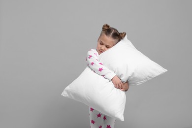 Girl in pajamas hugging pillow on gray background, space for text