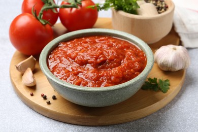 Photo of Homemade tomato sauce in bowl and fresh ingredients on light grey table, closeup