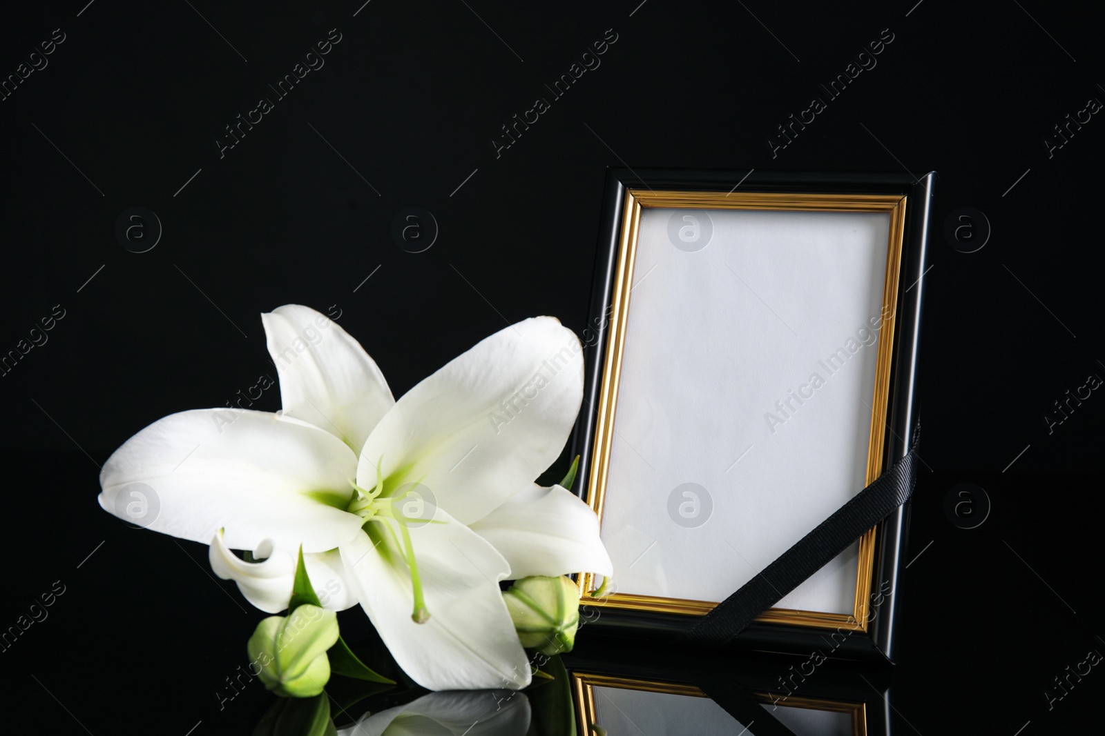 Photo of Funeral photo frame with ribbon and white lily on black table against dark background. Space for design