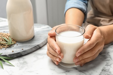 Photo of Woman with glass of hemp milk at white marble table, closeup