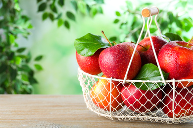 Ripe red apples in metal basket on wooden table against blurred background. Space for text