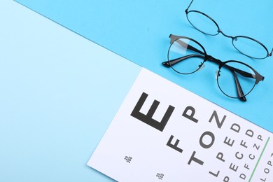 Photo of Vision test chart and glasses on light blue background, flat lay. Space for text