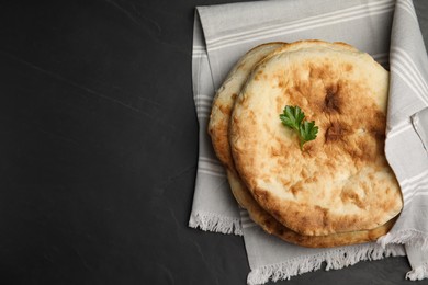 Photo of Delicious fresh pita bread with napkin on black table, top view. Space for text