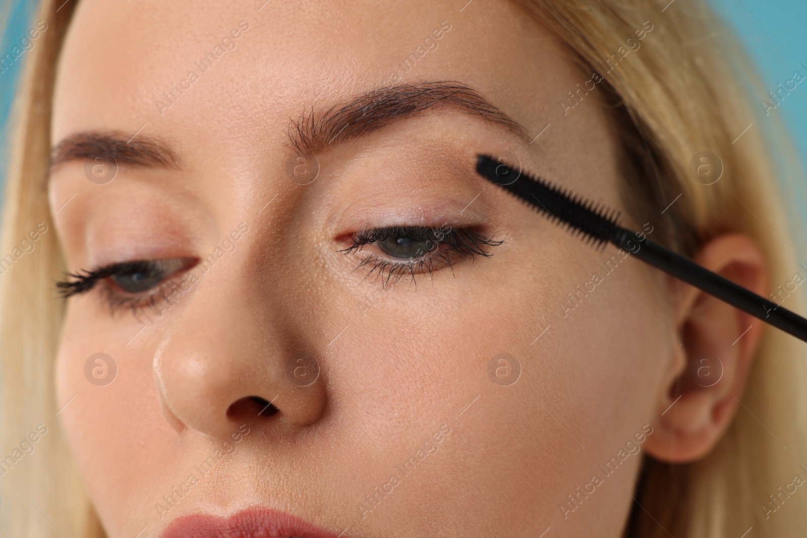 Photo of Beautiful woman applying mascara on light blue background, closeup