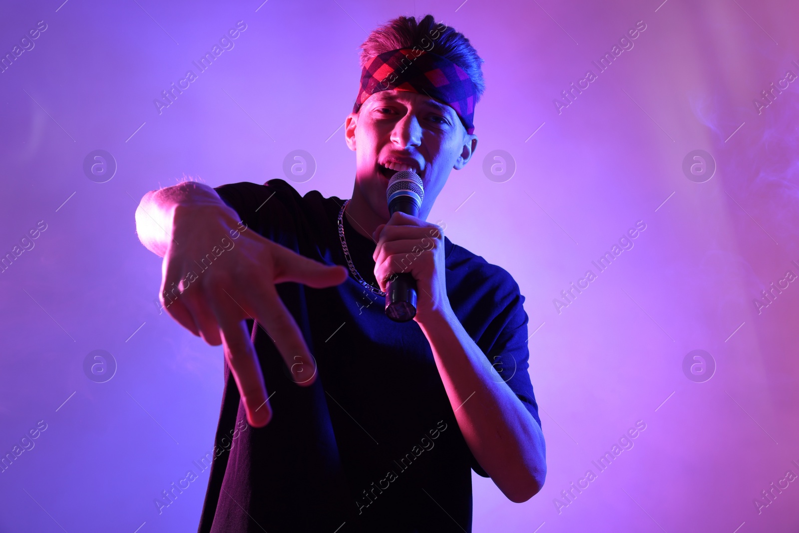 Photo of Stylish young man singing on color background in neon lights