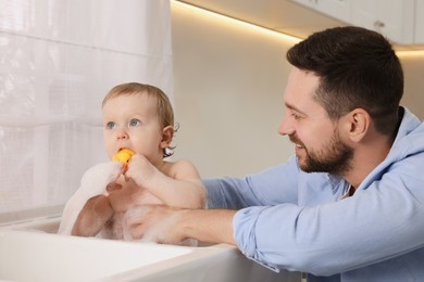 Father washing his little baby in sink at home
