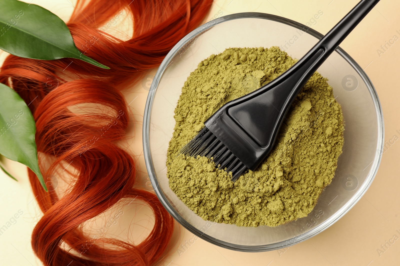 Photo of Bowl of henna powder, brush, green leaves and red strand on beige background, flat lay. Natural hair coloring
