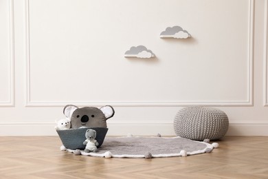 Photo of Wicker basket, toys and pouf near white wall indoors. Interior design