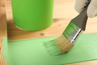 Worker applying green paint onto wooden surface, closeup