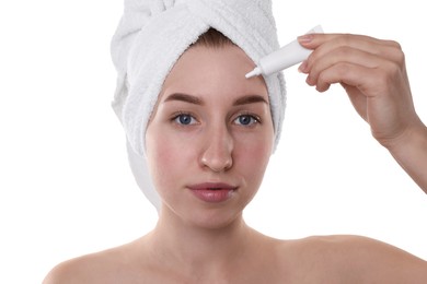 Photo of Young woman with acne problem applying cosmetic product onto her skin on white background