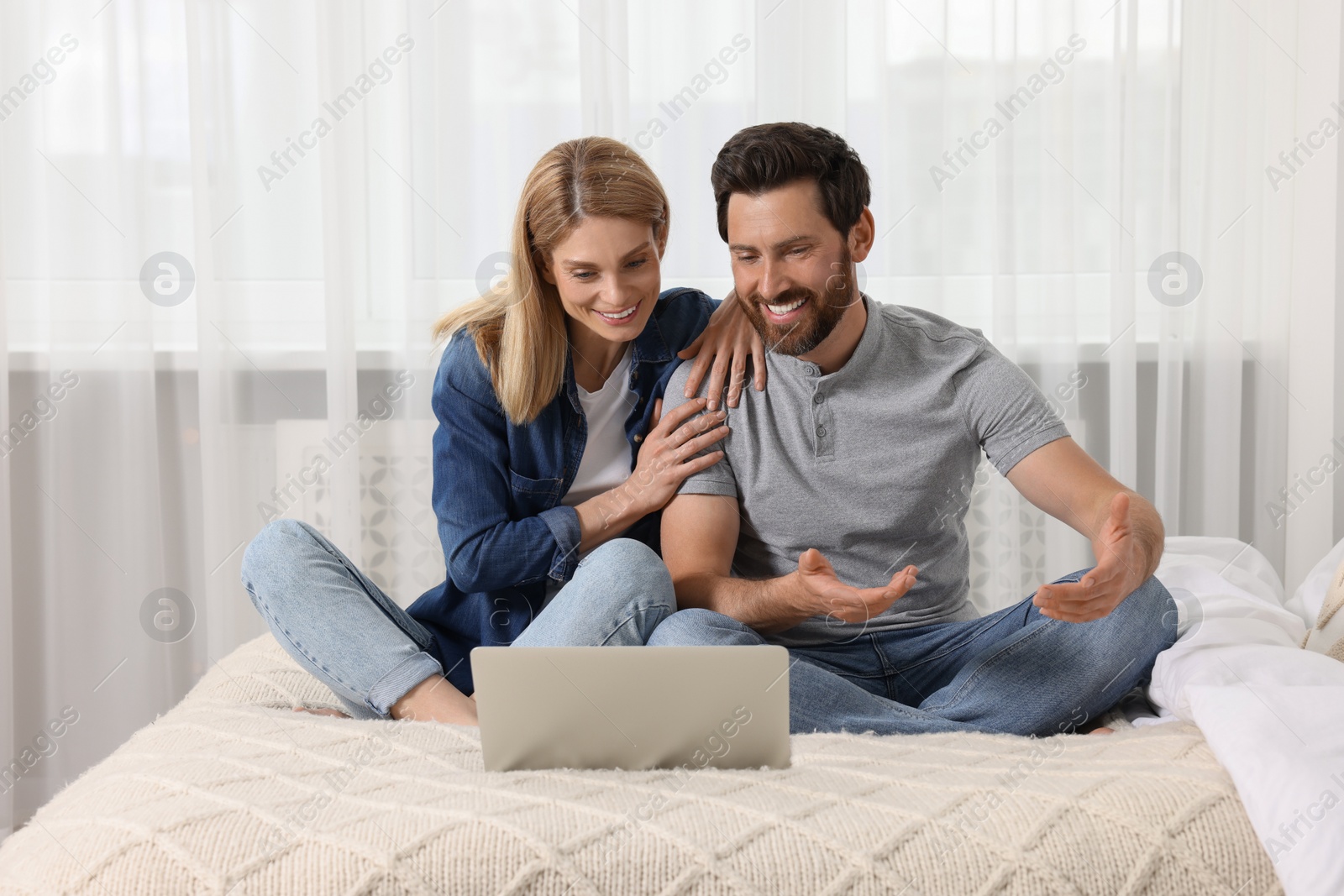 Photo of Happy couple with laptop on bed at home